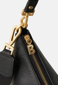 Bolso de cuero negro con una cremallera y herrajes dorados. Presenta una superficie texturada, un tirador de cremallera prominente con una etiqueta de 'B', y un robusto punto de unión para la correa.