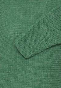 Tissu tricoté vert foncé avec un tissage texturé. Présente une manche visible aux bords légèrement effilochés et une apparence douce.