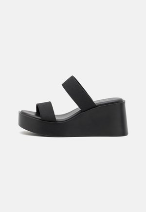 Sandales plateformes noires avec deux larges brides élastiques, une semelle anatomique et un talon compensé solide. Fabriquées en matière synthétique lisse.