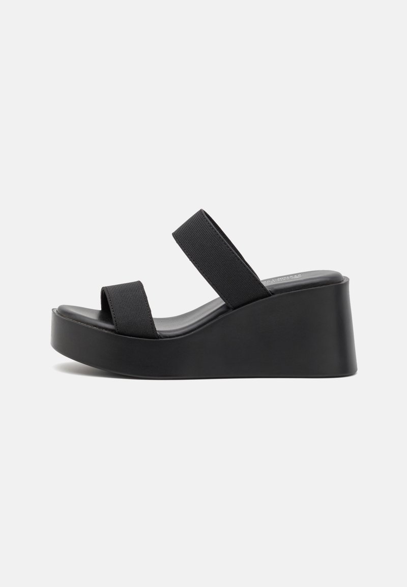 Sandales plateformes noires avec deux larges brides élastiques, une semelle anatomique et un talon compensé solide. Fabriquées en matière synthétique lisse.