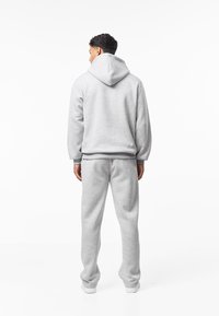 Harmaa huppari, jossa kiristettävä huppu ja resorireunukset hihoissa ja helmassa. Yhdistetty samansävyisiin jogger-housuihin, molemmat pehmeästä kankaasta ja rento istuvuus.