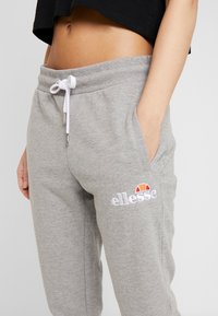 Grå mjukisbyxor i mjukt material med dragsko i midjan. Har sidofickor och en broderad "ellesse"-logotyp i vitt och orange.