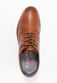 Chaussure en cuir marron avec une surface texturée, forme de bout rond, six œillets pour les lacets, et un intérieur doublé en tissu avec une semelle intérieure rembourrée.