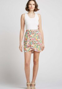 Jupe portefeuille florale ornée de motifs de feuilles multicolores éclatants, en tissu doux, avec un ourlet asymétrique, associée à un débardeur ajusté blanc.