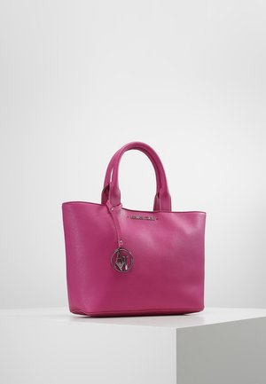 Roze leren handtas met dubbele handvatten en een ronde metalen hanger die aan één handvat hangt, geplaatst op een witte ondergrond tegen een neutrale achtergrond.