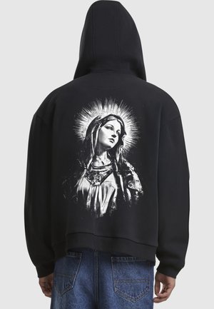 Czarna bluza z kapturem o skróconym kroju z białym nadrukiem graficznym przedstawiającym kobietę na tle efektu aureoli z tyłu. Miękka tekstura materiału.