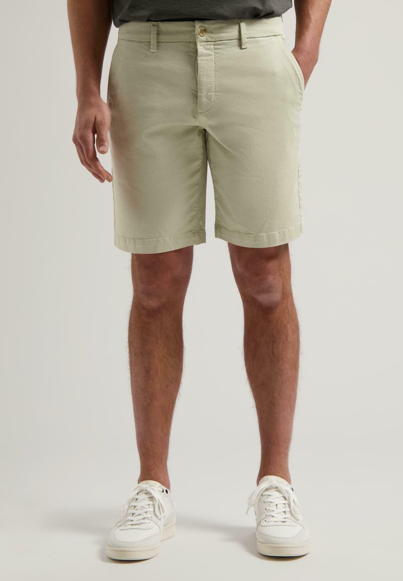 Shorts en coton vert clair avec une coupe plate, fermeture par bouton et poches latérales. Présente une texture lisse et des bords ourlés.