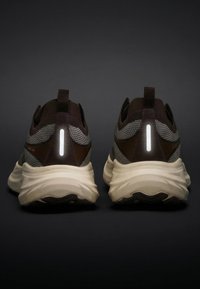 Een paar bruine en grijze sportschoenen gezien vanaf de achterkant met dikke beige zolen en verticale reflecterende strepen op de hielen.