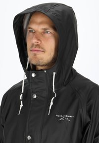 Czarna wodoodporna kurtka przeciwdeszczowa z kapturem, wyposażona w przedni zamek błyskawiczny, zatrzaski oraz białe sznurki do ściągania. Logo na lewej stronie klatki piersiowej.