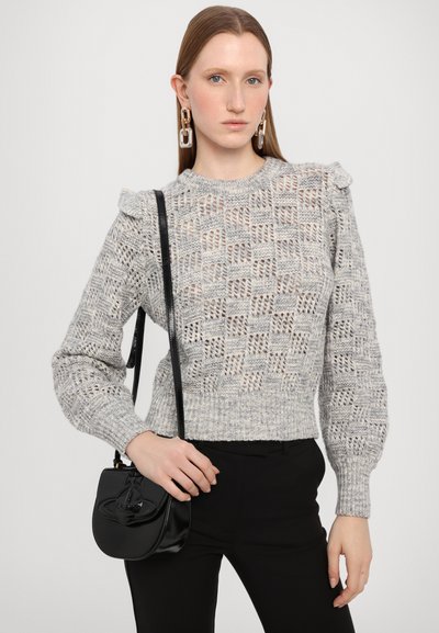 Pull en tricot gris avec des découpes à motifs, des manches bouffantes et un ourlet côtelé. Associé à un petit sac à bandoulière en cuir noir.