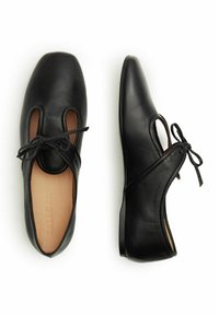 Ballerines en cuir noir avec un bout rond, présentant des côtés découpés et un accent de nœud lié. Texture lisse et semelle discrète.