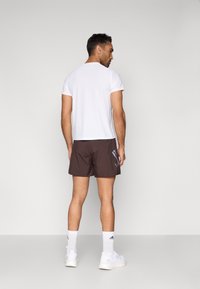 Ανδρικά αθλητικά ρούχα: λευκό πουκάμισο με κοντά μανίκια, καφέ σορτς με ρίγες στο πλάι, λευκές κάλτσες και αθλητικά παπούτσια. Λείο ύφασμα και αθλητική εφαρμογή.