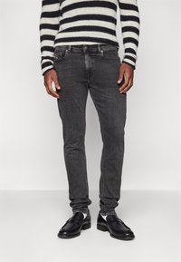 Jeans gris oscuro con un corte ajustado, con un ligero desgaste y un diseño clásico de cinco bolsillos, combinados con zapatos de cuero negros y un suéter a rayas.