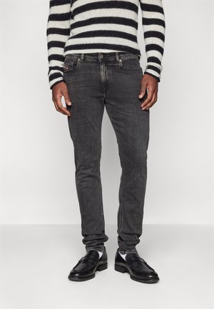Jeans gris foncé avec une coupe slim, présentant une décoloration subtile et un design classique à cinq poches, associés à des chaussures en cuir noires et un pull rayé.