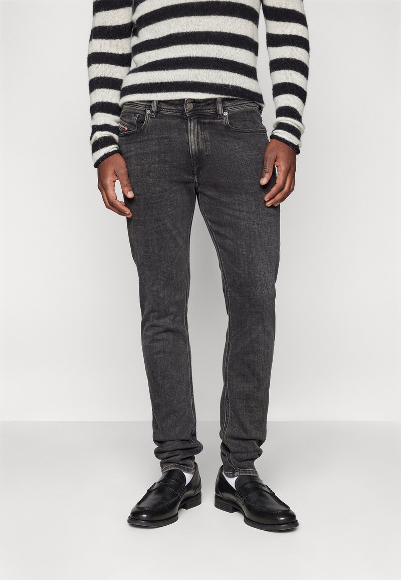 Jeans gris oscuro con un corte ajustado, con un ligero desgaste y un diseño clásico de cinco bolsillos, combinados con zapatos de cuero negros y un suéter a rayas.