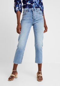 Ljust blå cropped jeans i denim, med en klassisk femficksdesign och hög midja, matchade med nudefärgade blockklacksandaler.