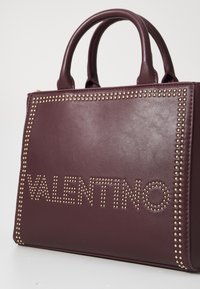 Bordeauxfarbene Lederhandtasche mit genieteten Akzenten und prägierter "VALENTINO"-Schrift. Doppelte Griffe und strukturiertes Design. Glatte Textur.
