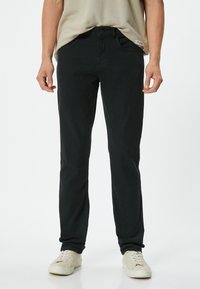 Mustat, slim-fit-housut pehmeästä kankaasta; sisältää viisi taskua, ommeltuja yksityiskohtia ja nappisulkemisen. Yhdistetty valkoisiin kenkiin.