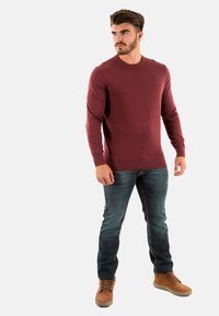 Maglione a maglia borgogna con maniche lunghe, scollatura rotonda e polsini a coste, abbinato a jeans in denim blu e stivali marroni con lacci.