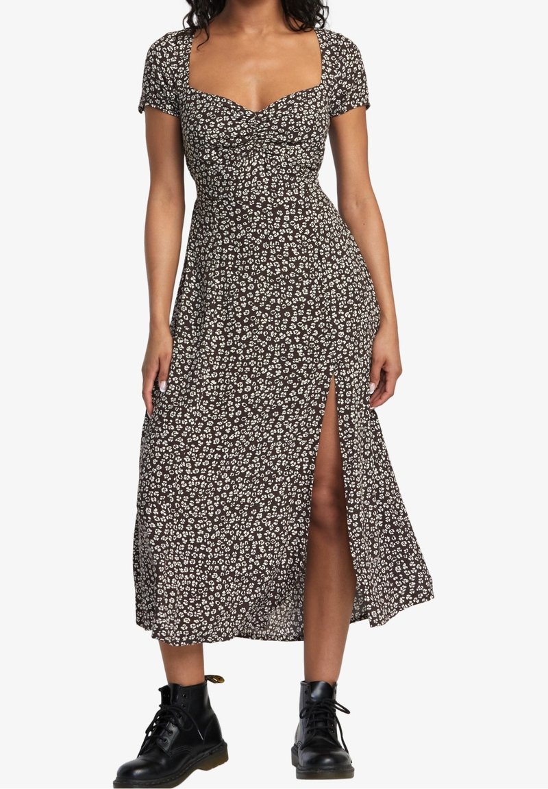 Femme portant une robe midi noire à motifs floraux avec des manches courtes et une fente à l'avant, accompagnée de bottines noires à lacets.