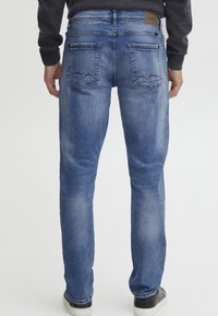 Jeans de mezclilla azul de lavado medio, diseño de pernera recta, con dos bolsillos traseros con costura en zig-zag y una etiqueta de logo en la cintura.