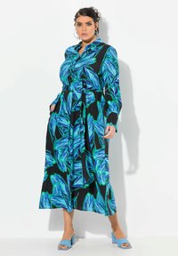 Svart klänning med tryck av blå och gröna löv, långa ärmar, knäppning framtill, matchande bälte och mittlång nederkant. Kombinerad med blå klackar.