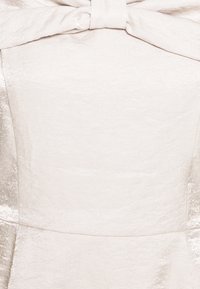 Vestido de color claro con una tela suave y texturizada que tiene un acabado satinado. Incluye un destacado detalle de lazo en el escote para añadir interés al diseño.