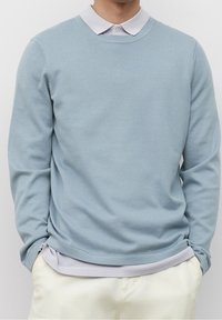 Pullover azzurro chiaro realizzato in materiale morbido, con maniche lunghe e scollatura rotonda, indossato sopra una camicia colletto grigia chiara.