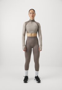 Lys brun langermet crop topp med glidelås, parret med rillede mørkebrune høytaljede leggings og svarte joggesko med hvite sokker.