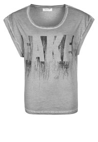 Camiseta de manga corta gris con la palabra "FAKE" impresa en grandes letras negras desgastadas en el frente. Tejido suave con un corte holgado.