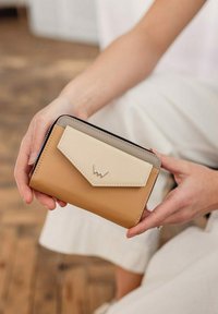 Bifold peněženka v hnědé a krémové kůži s šedým klopním víkem, zdobená kovovým emblémem a zipovým uzávěrem. Kompaktní, obdélníkový design.