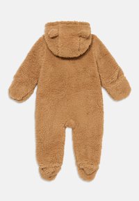 Romper de bebé de felpa marrón con capucha que presenta pequeñas orejas de oso y cubre pies incorporados, mostrado plano sobre un fondo blanco.