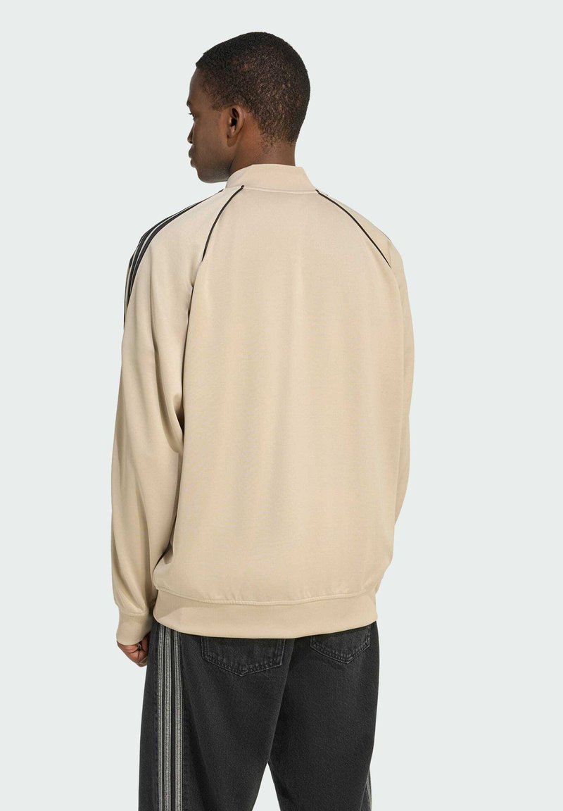 Beige sweatshirt met een hoge kraag en zwarte randdetails. Zachte textuur, losse pasvorm en zichtbare naden. Gecombineerd met donkere broeken met strepen.
