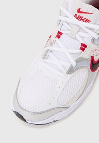 Nike tenisice s gornjim dijelom od bijele mrežice, srebrnim akcentima, crvenim šavovima i crnim logotipom swoosh. Dizajn s vezanjem i podstavljenim ovratnikom.