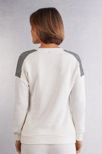 Vitt ribbat sweatshirt med svart rutigt mönster på axlarna och tighta ärmslut. Mjukt tyg med en avslappnad passform, detaljerade sömmar synliga.