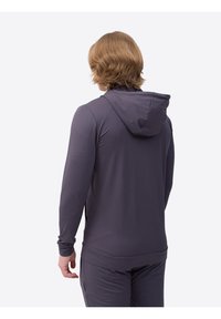 Grauer sportlicher Kapuzenpullover mit strukturiertem Stoff, langen Ärmeln und Kordelzugkapuze. Die Person trägt passende graue Hosen.