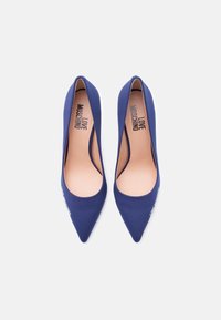 Ζευγάρι από ψηλοτάκουνα παπούτσια μπλε ναυτικού με μυτερή μύτη, με την επιγραφή "LOVE MOSCHINO" στο εσωτερικό και στην εξωτερική πλευρά του μπροστινού μέρους κάθε παπουτσιού.