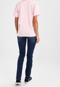 Světle růžové bavlněné tričko s krátkým rukávem, volný střih; v kombinaci s tmavě modrými slim-fit džíny a černými teniskami.