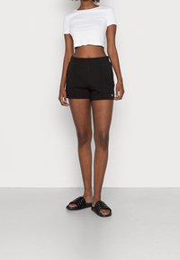 Černý cropped top spárovaný s černými, texturovanými sportovními šortkami s elastickým pasem. Nošeno s černými sandály na pásky.