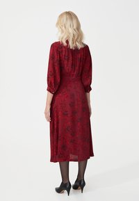 Pitkähihainen viininpunainen mekko, jossa on kukkakuosi, napit käsivarressa, valuva kangas ja polvipituus. Yhdistetty mustiin korkeakorkoisiin kenkiin.