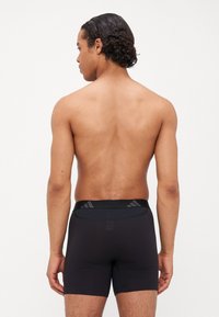 Boxer briefs pretos com uma textura suave, cintura elástica com detalhes de padrão sutis e um design ajustado. Vista traseira apresentada.