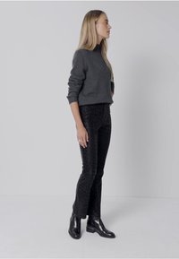 Pull en tricot gris, pantalon noir à imprimé léopard ajusté, et bottines noires. Texture lisse, coupe slim, et détails de motif subtils.