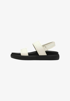 Sandales en cuir blanc avec deux brides réglables, semelle noire et forme arrondie. Texture lisse, couture minimale et design de talon sécurisé.