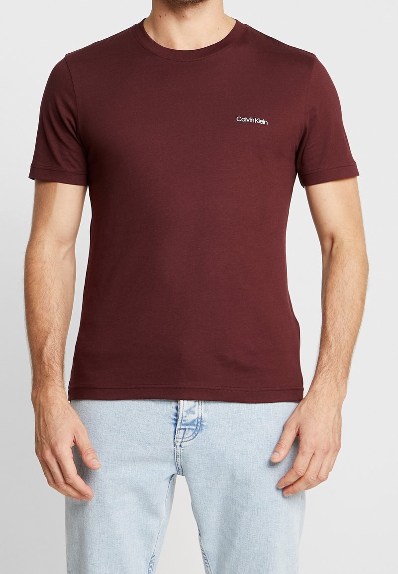 Bordeaux katoenen T-shirt met korte mouwen en een ronde hals. Heeft een klein wit Calvin Klein-logo op de borst.