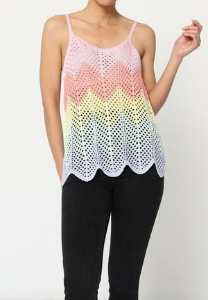 Débardeur léger en maille ouverte, pastel, avec un motif en chevrons ; doté de bretelles spaghetti et d'un ourlet festonné. Porté par-dessus un jean noir.