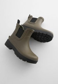 Bottes en caoutchouc olive avec des panneaux latéraux élastiques noirs, une semelle texturée et un design à bout rond pour l'adhérence et la stabilité.