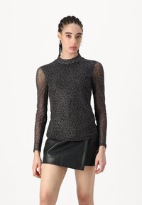 Crna bluza dugih rukava s prozirnim uzorkom leopard, visokim ovratnikom i prilagođenim krojem, u kombinaciji s crnom mini suknjom od umjetne kože.