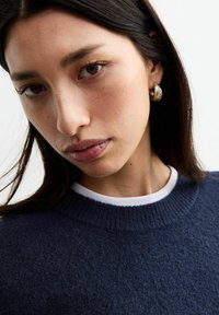 Pull en maille bleu marine avec tissu texturé, doté d'un col rond côtelé et d'un col intérieur blanc, accompagné de boucles d'oreilles dorées.
