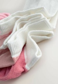 Valged ja roosad pehmed soonikkoega kudum-sokid, mis on kerge pinna peal kattuvana laotatud, näidates voltimist ja kangast detaili.