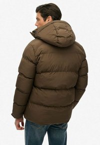 Brun pufferjakke med hætte, der har quiltede sektioner til isolering. Materialet ser glat og let blankt ud.